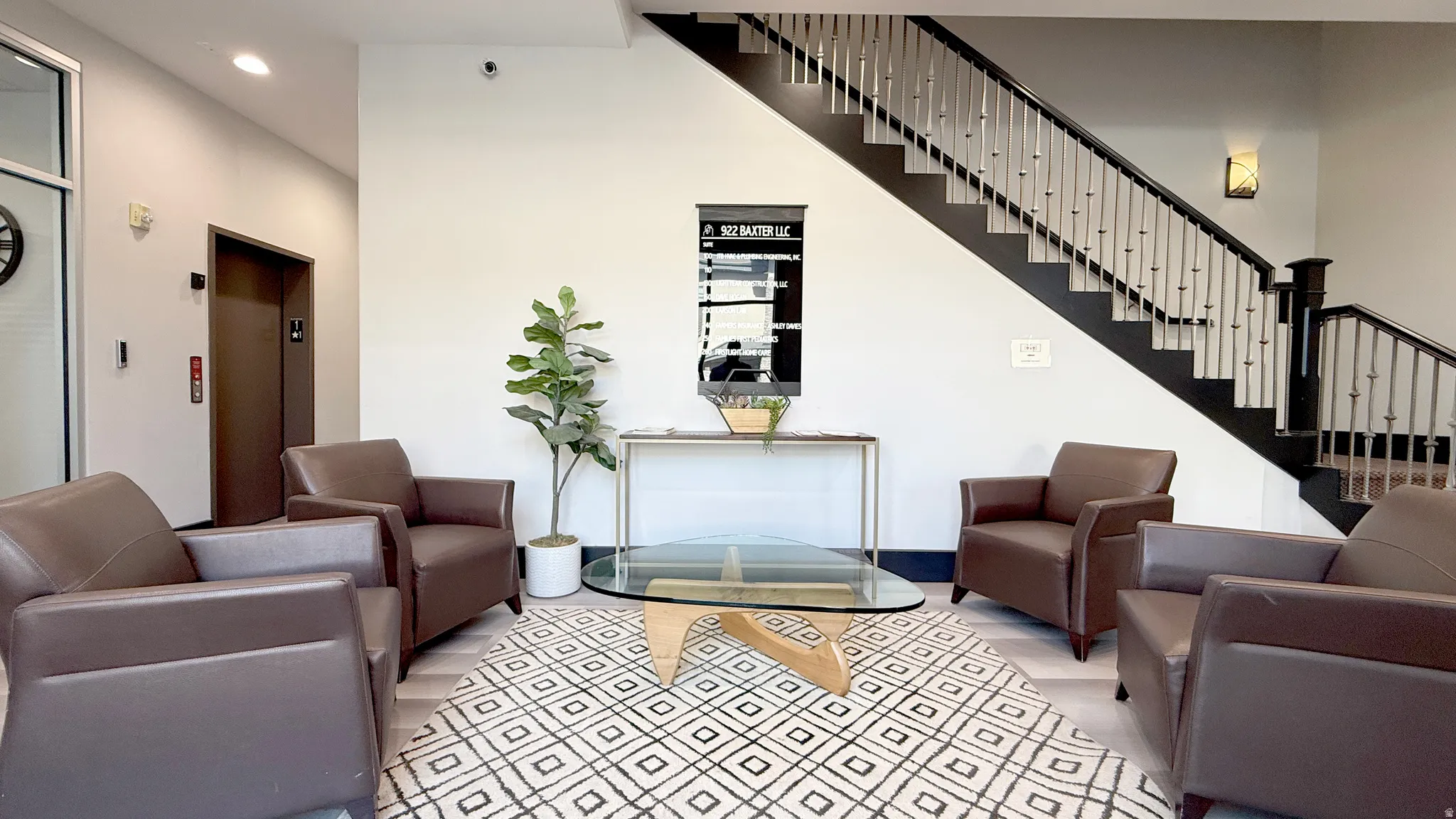 Inviting lobby featuring a prominent staircase with iron balusters, light wood-finish flooring, and an elevator for accessibility
