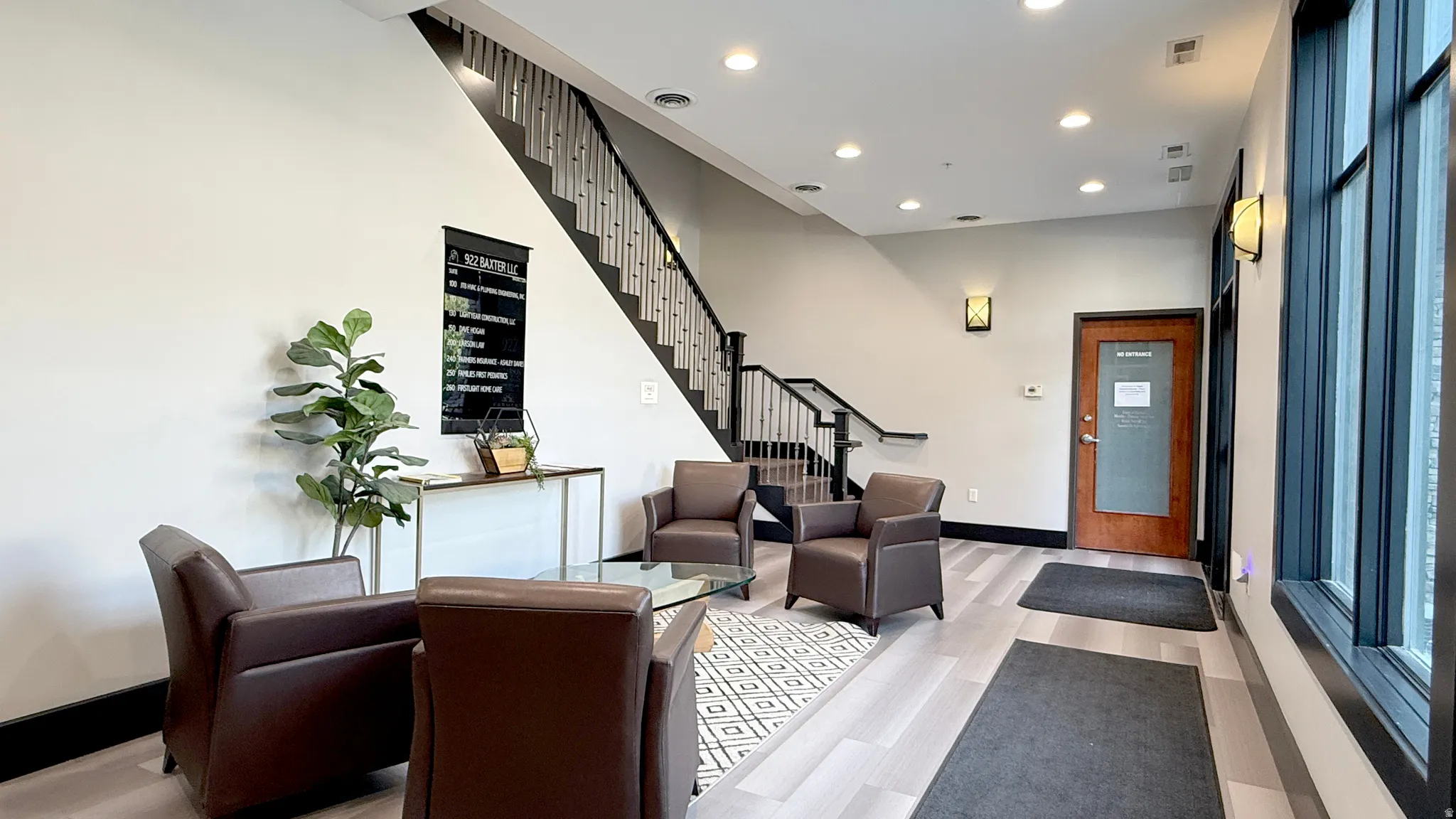 Lobby area featuring wood-finish flooring, a dark wood and metal staircase, recessed lighting, large windows, and wall sconces