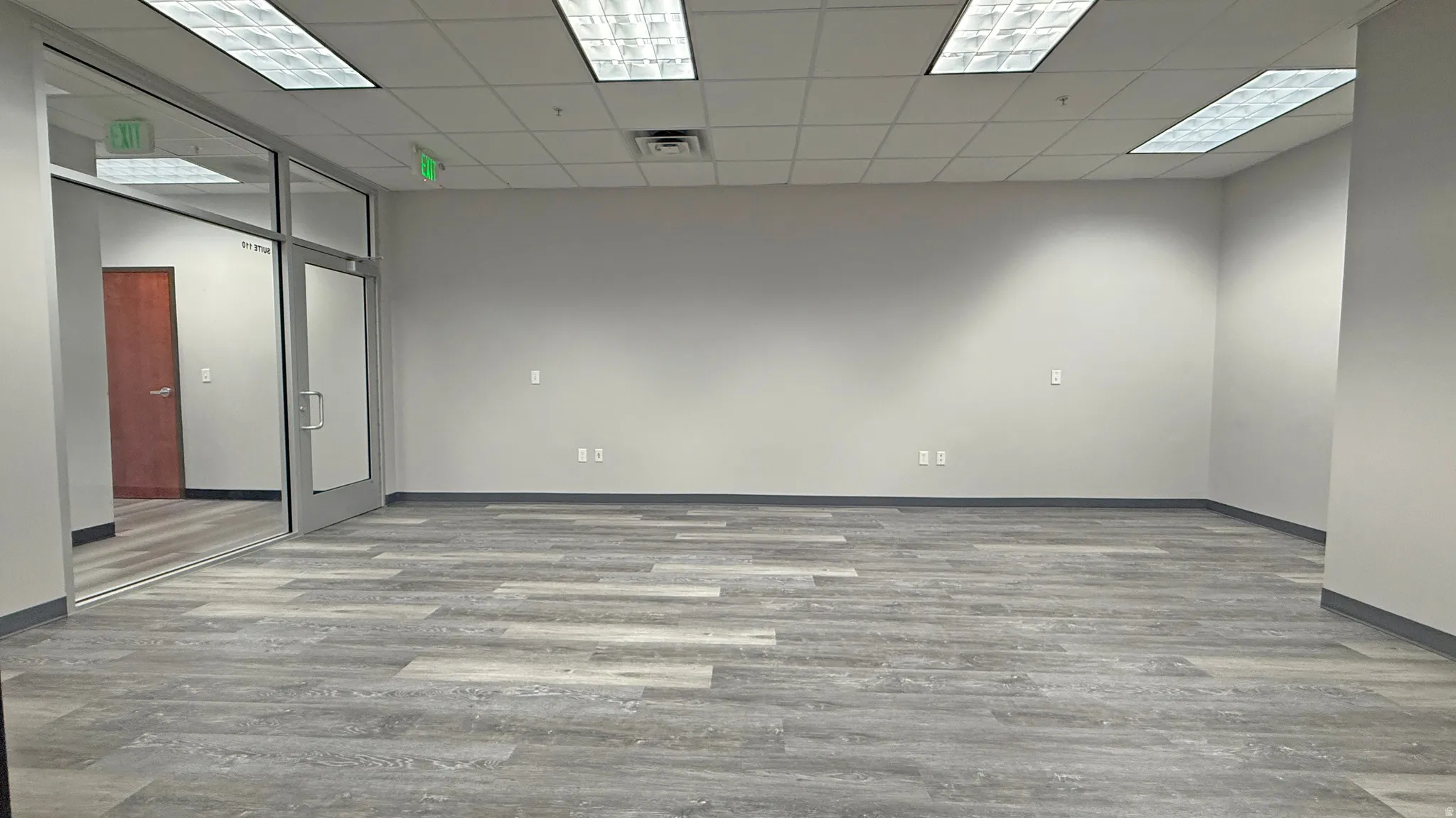 Spacious interior with neutral walls, wood-finish flooring, and a drop ceiling with recessed fluorescent lighting