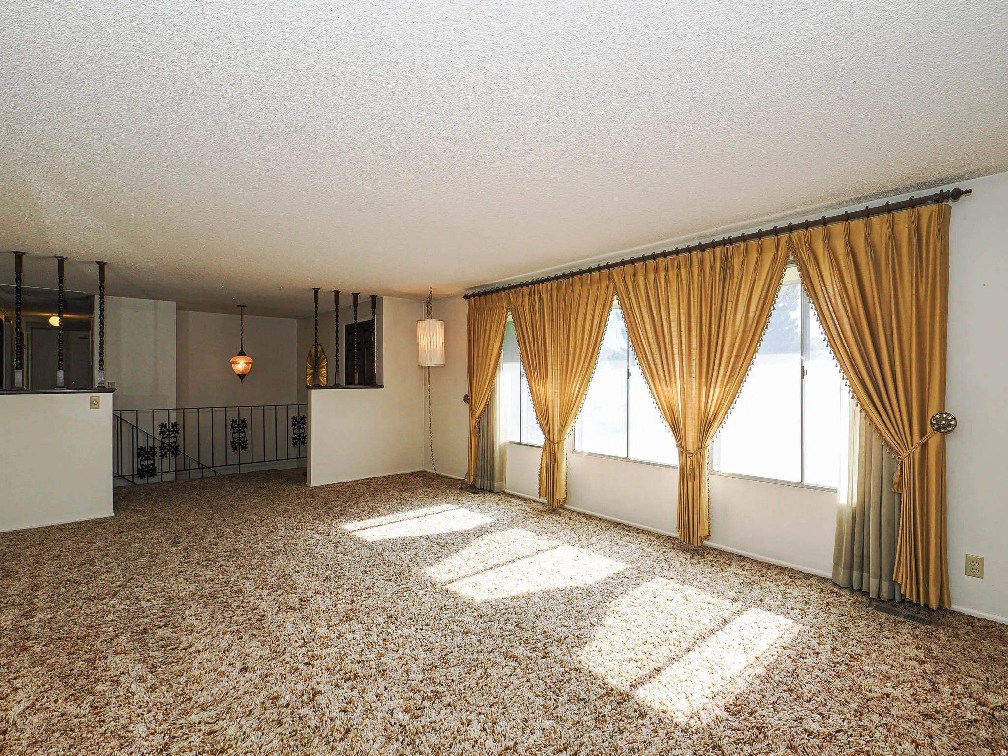 Spacious living area featuring expansive windows with drapery, textured carpeting, and a decorative railing