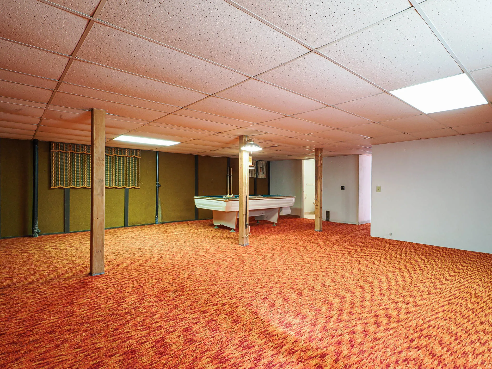 Expansive finished basement featuring patterned carpeting, drop ceiling with recessed lighting, and exposed structural columns