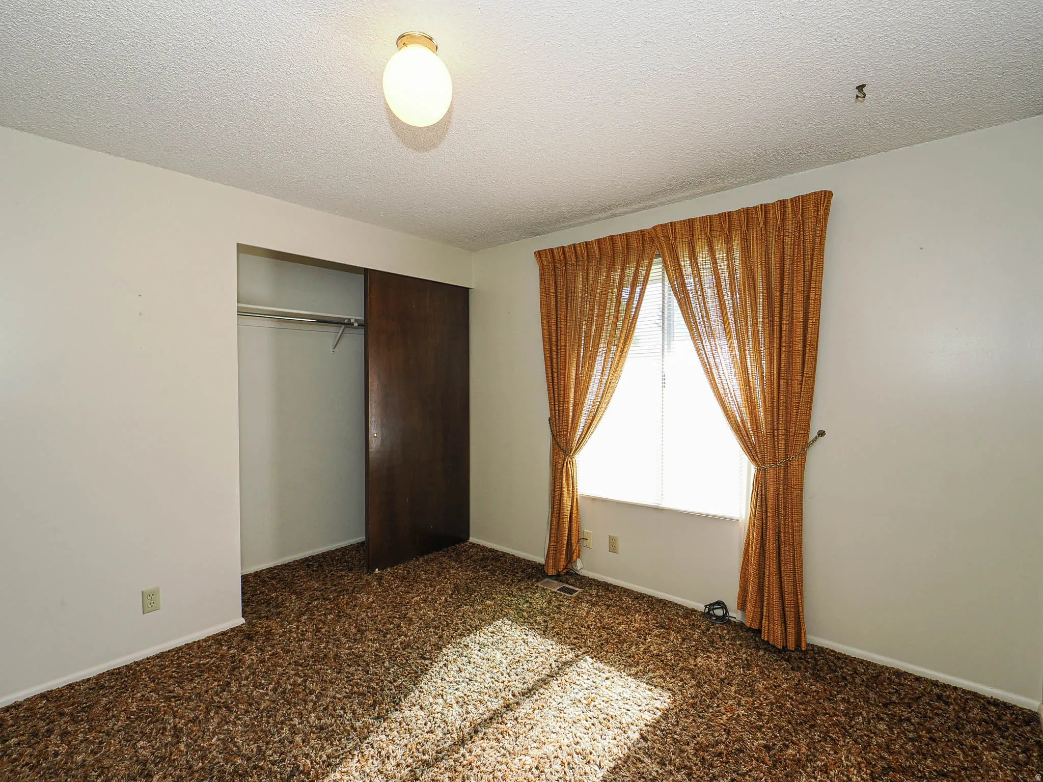 Carpeted room with a window, white walls, and a built-in closet featuring a dark wood sliding door