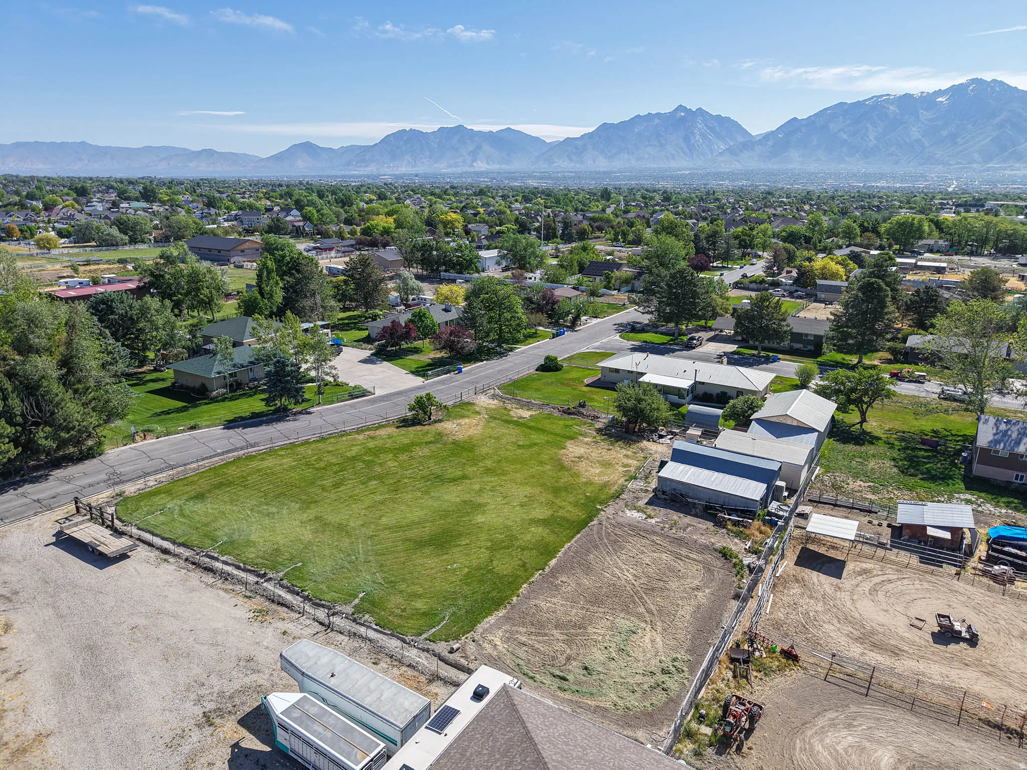 Expansive undeveloped land parcel featuring a grass field and a partially fenced dirt area, set against a backdrop of distant mountains