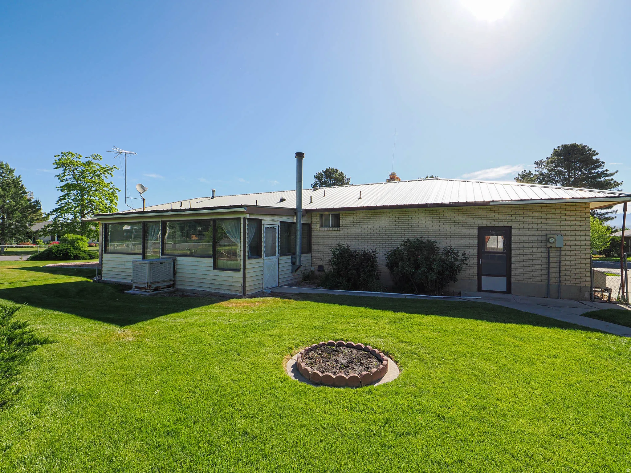 Expansive green lawn with a round stone planter, complemented by a screened-in porch with multiple windows, a light brick exterior, and a metal roof