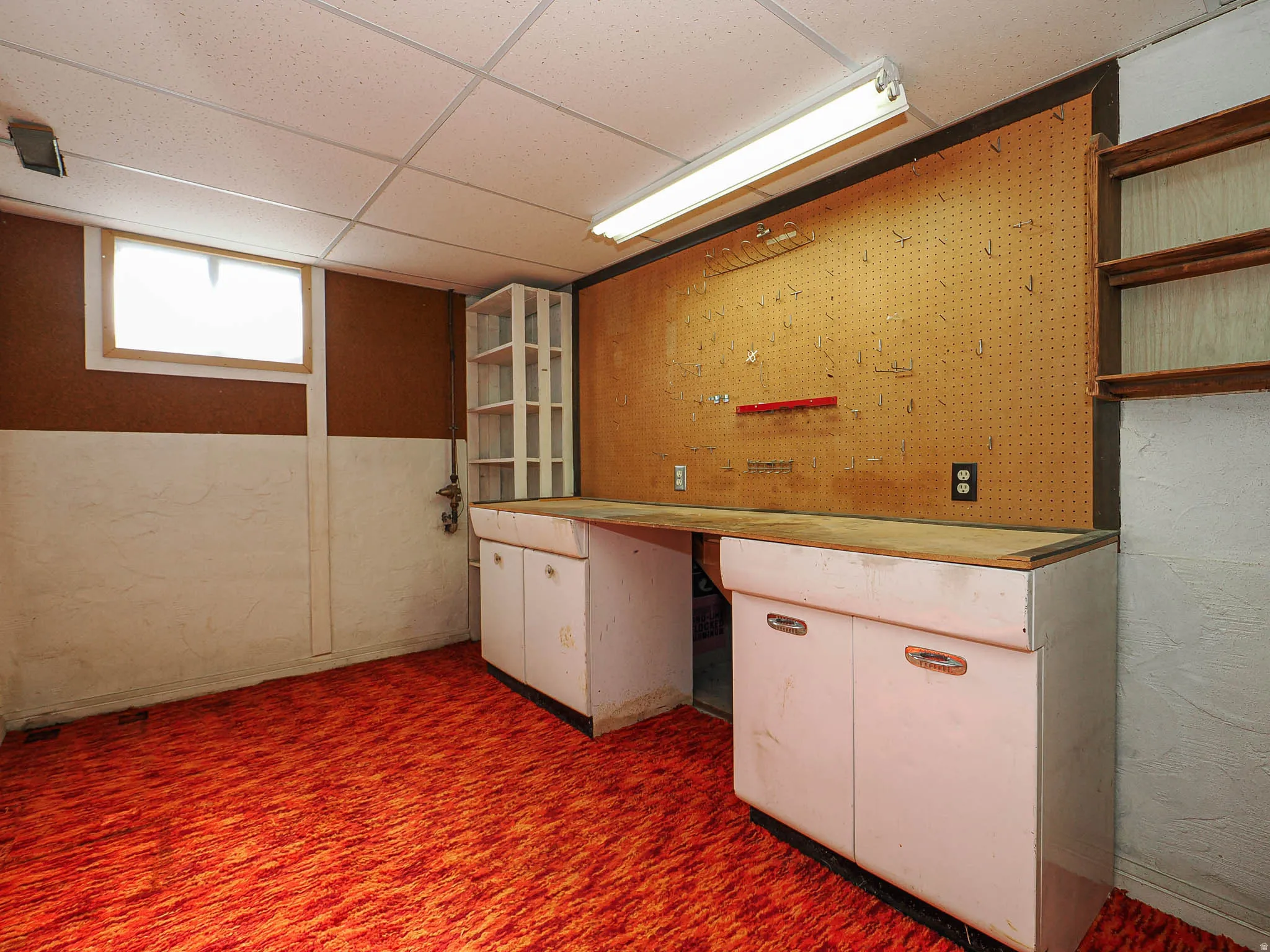 Workroom area featuring a built-in workbench with storage cabinetry, pegboard wall, overhead fluorescent lighting, and a drop ceiling