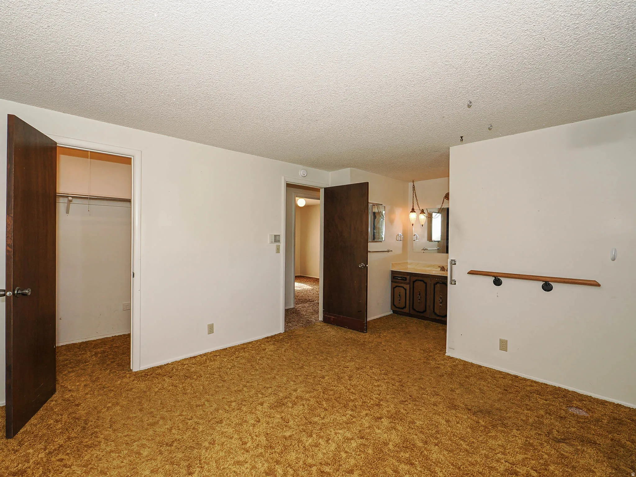 Room featuring textured ceiling, plush gold carpet, and a built-in closet with hanging rod