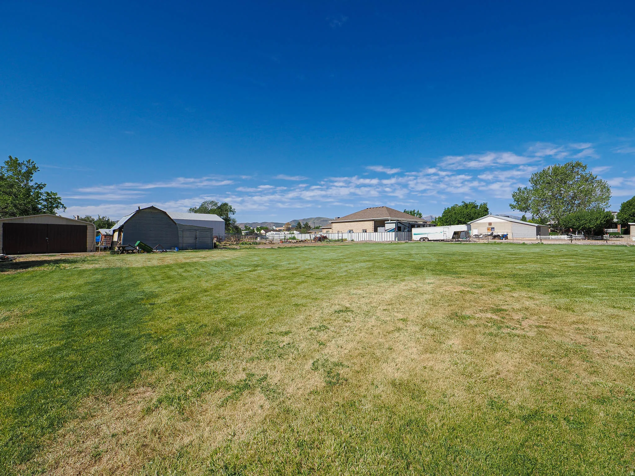 Expansive, flat grassy lot with a brown metal storage shed and a gray barn-style outbuilding