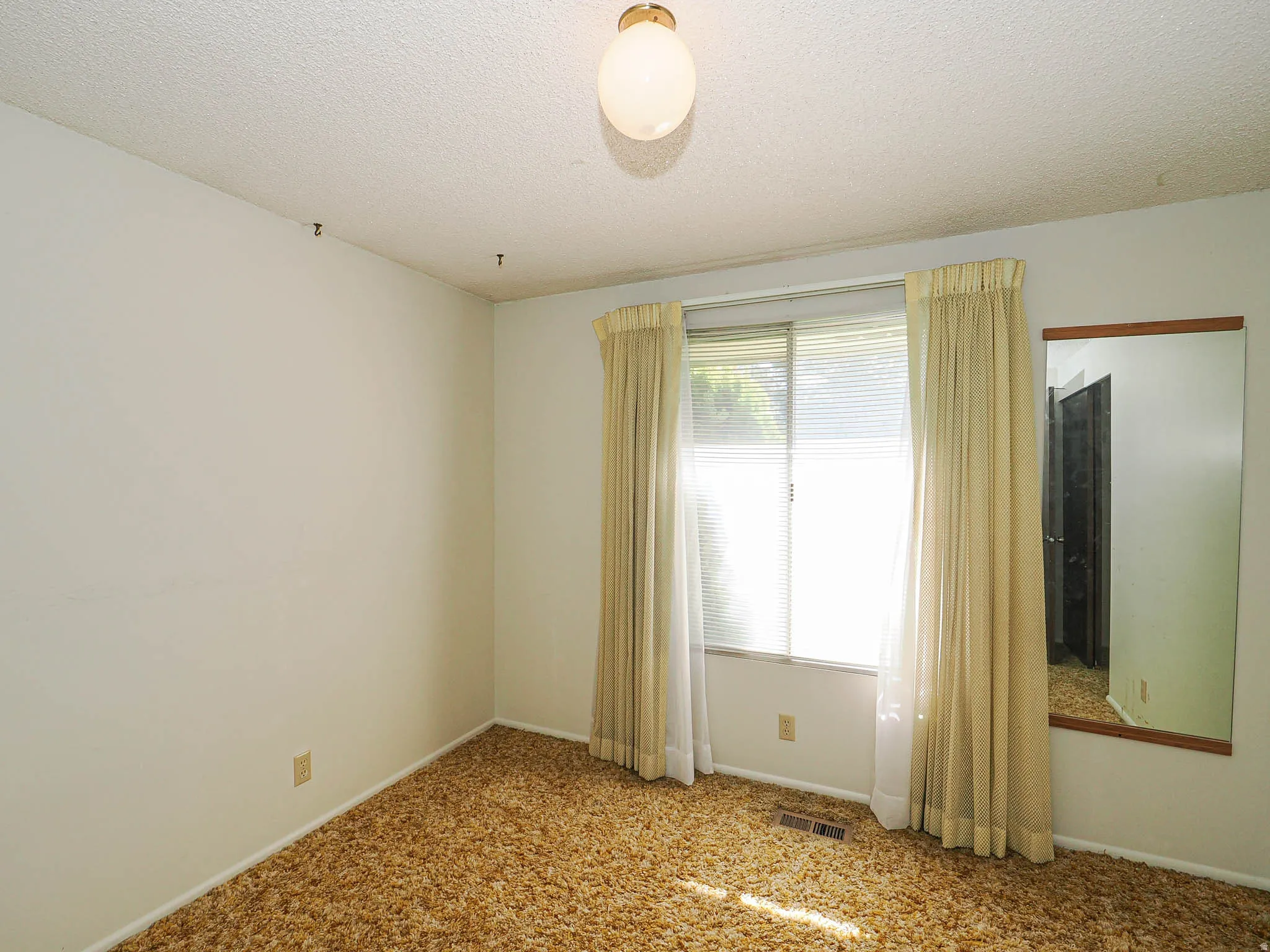 Room featuring a window with blinds and drapes, a wall-mounted mirror, and wall-to-wall carpeting