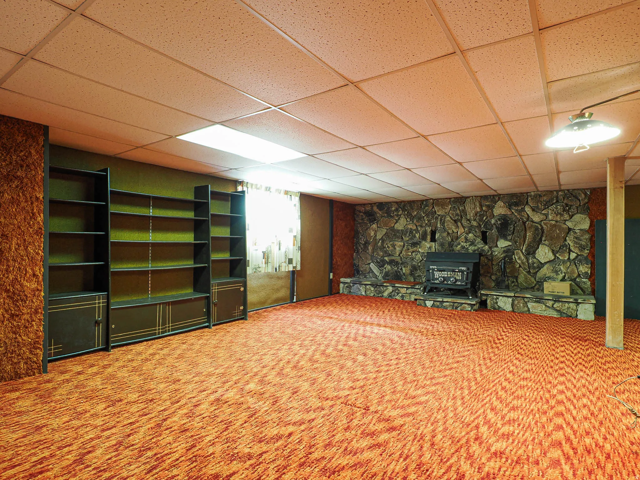 Spacious room featuring a stone-faced hearth with an insert, extensive patterned carpeting, built-in shelving units, and a drop ceiling with recessed lighting