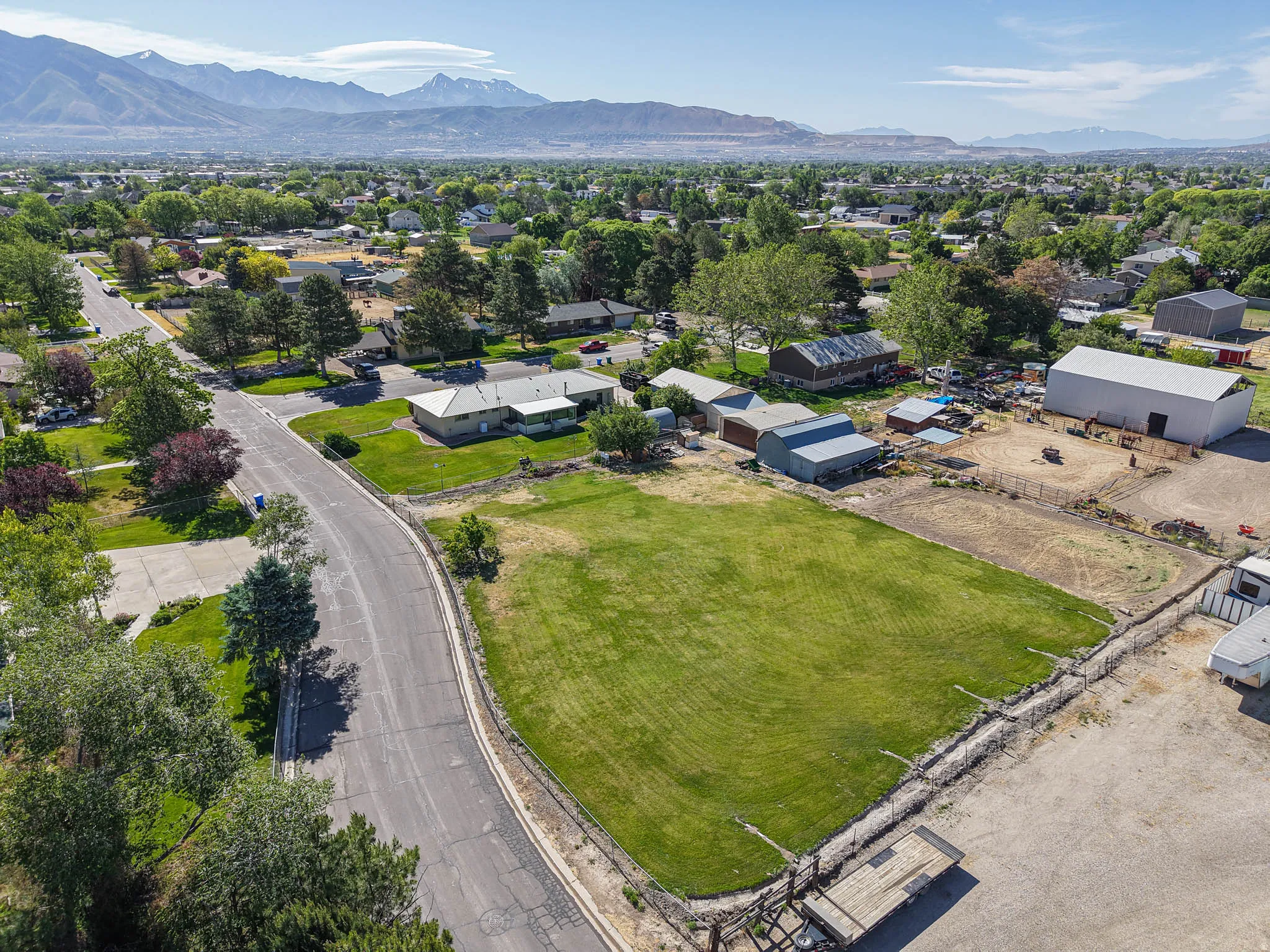 Expansive green lot featuring a mountain backdrop, a paved road, and established landscaping