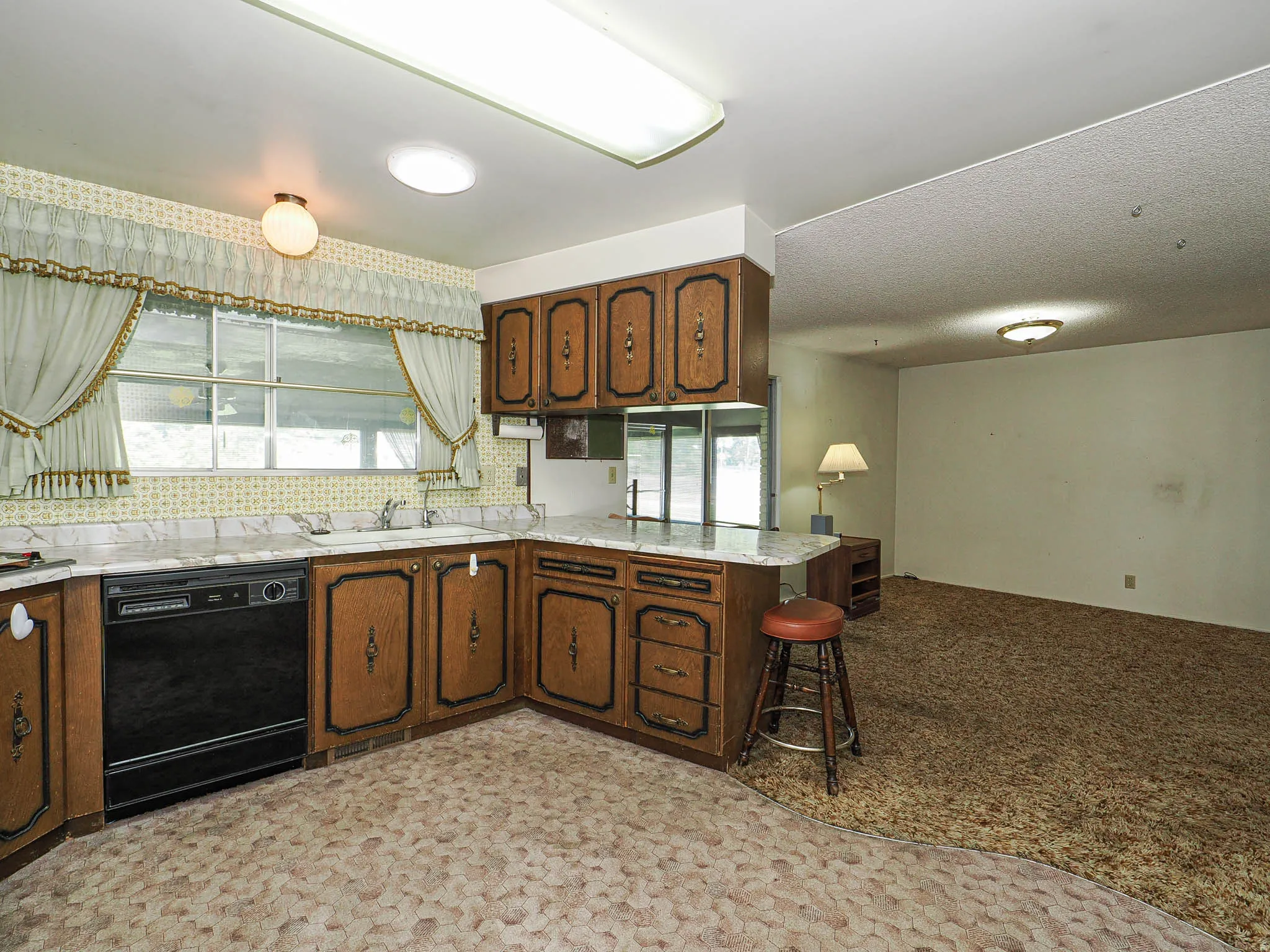 Kitchen with wood-finish cabinetry, light-toned countertops, and a built-in black dishwasher