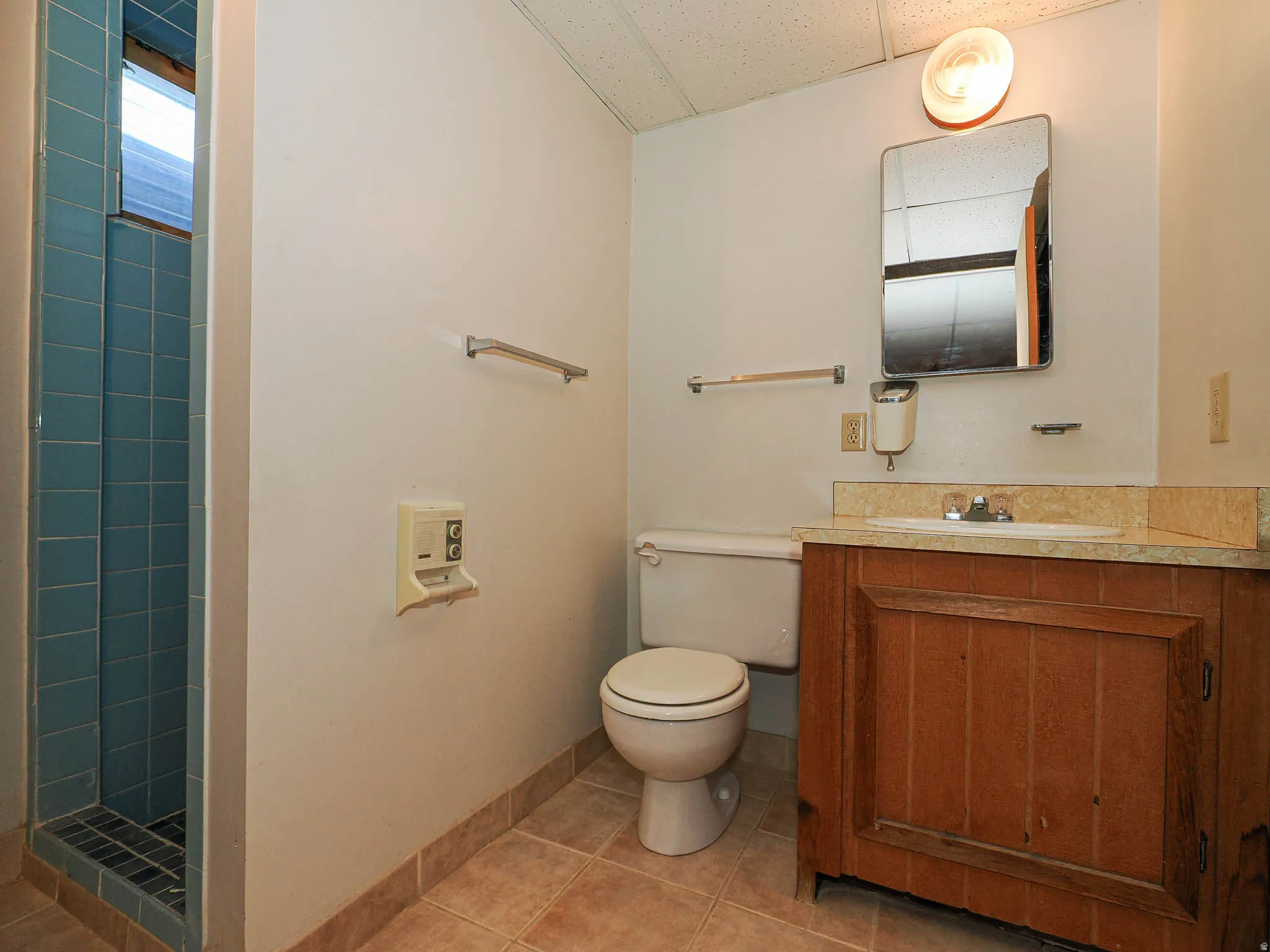 Bathroom featuring a standing shower with blue tile, a wood-finish vanity with an integrated sink and light-toned countertop, a wall-mounted mirror, and tile flooring