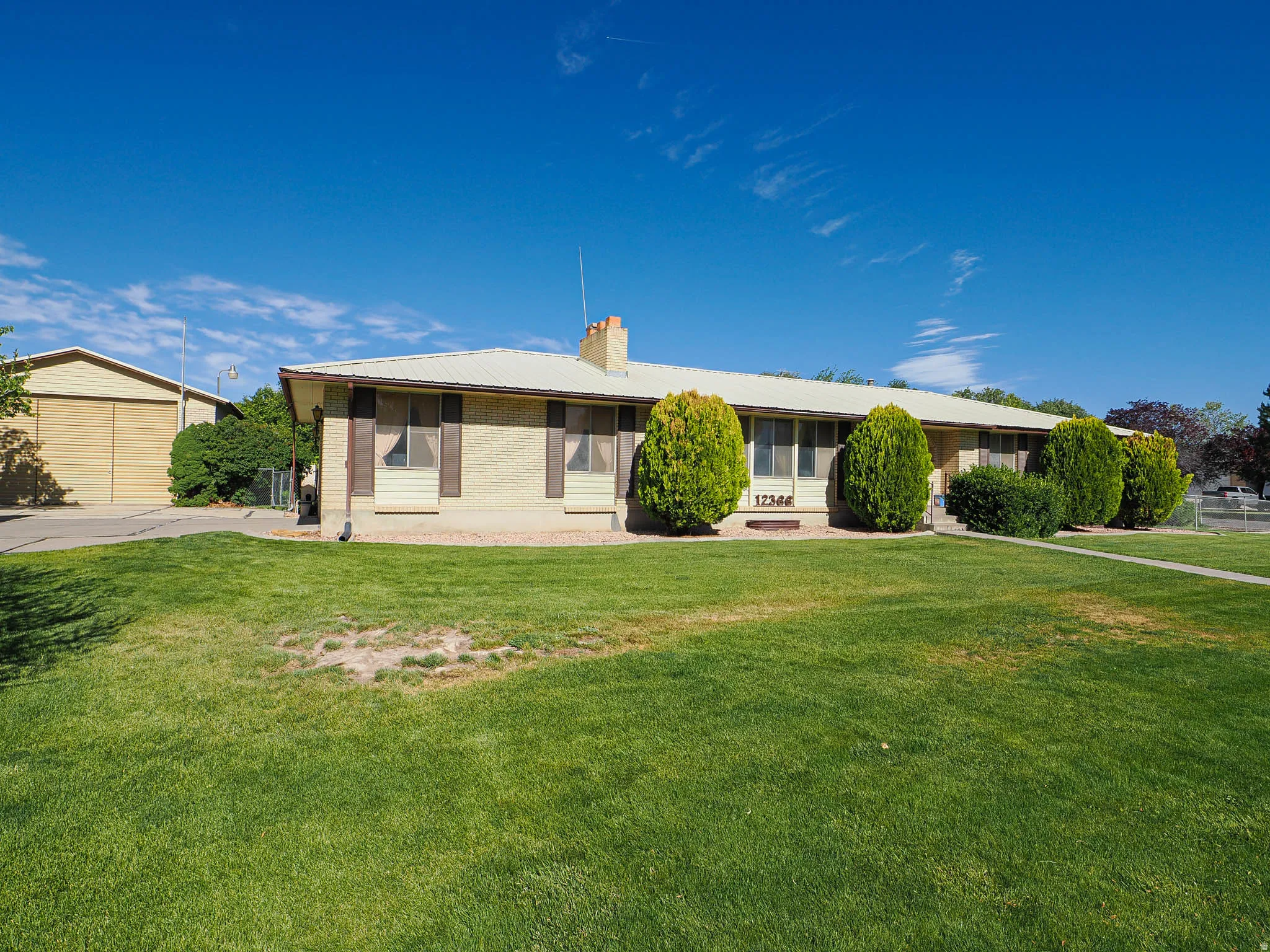Ranch-style residence featuring a light-colored brick exterior, brown shutters, and a metal roof