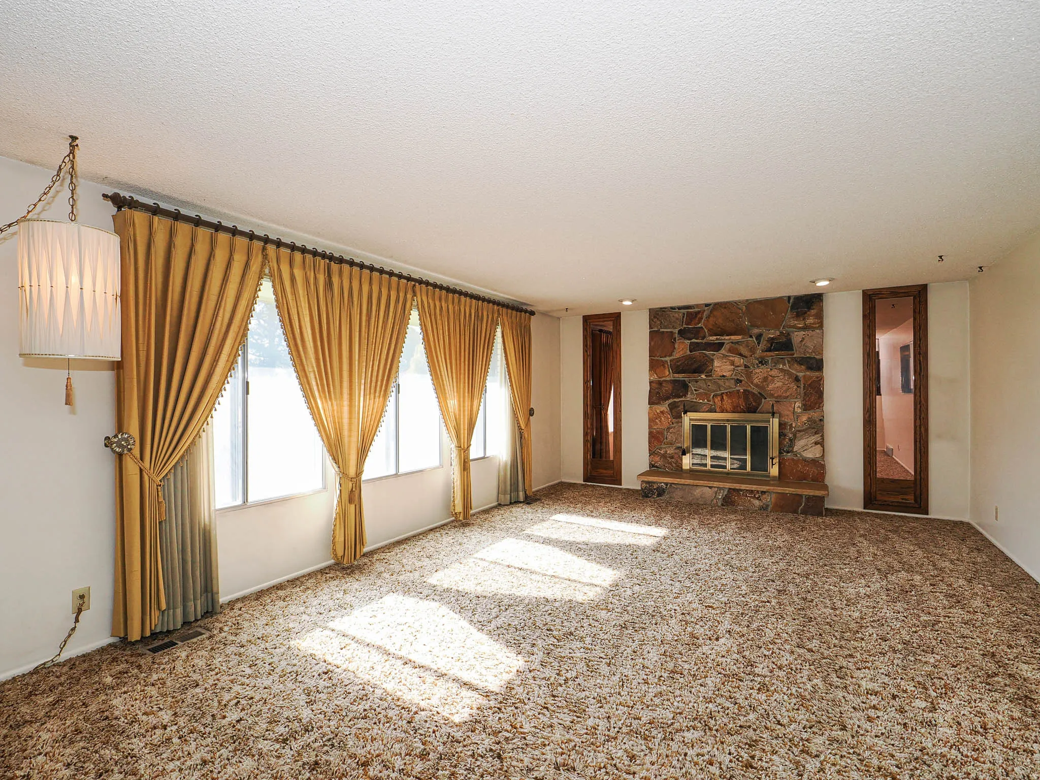 Spacious room featuring a stone-clad fireplace with hearth, multiple windows, recessed lighting, and a decorative ceiling fixture