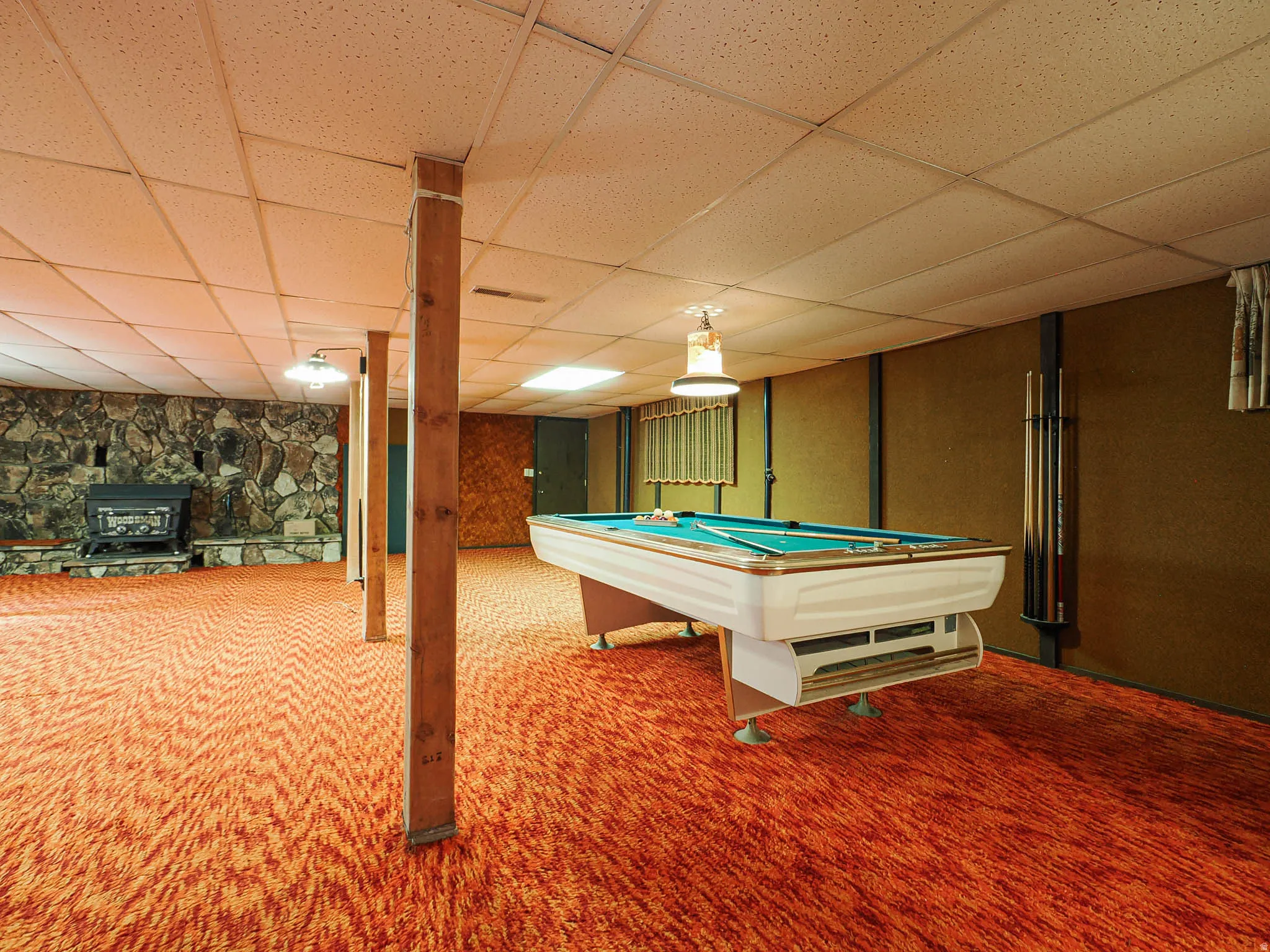 Recreation room featuring patterned orange carpet, stone accent wall, wood-paneled support beams, and recessed lighting