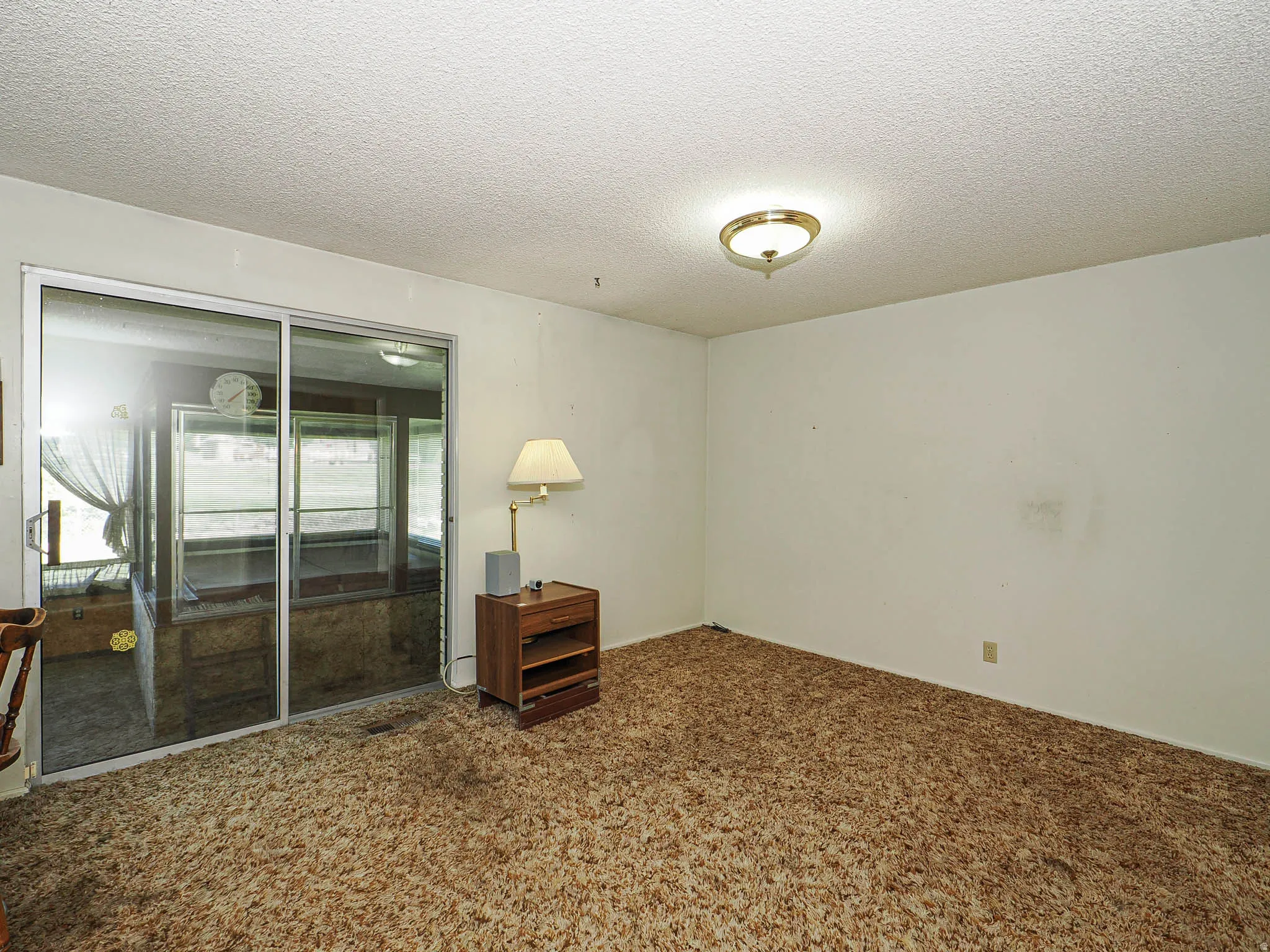 Sliding glass doors opening to an enclosed porch, textured ceiling, wall-to-wall carpeting, and a flush-mount ceiling light