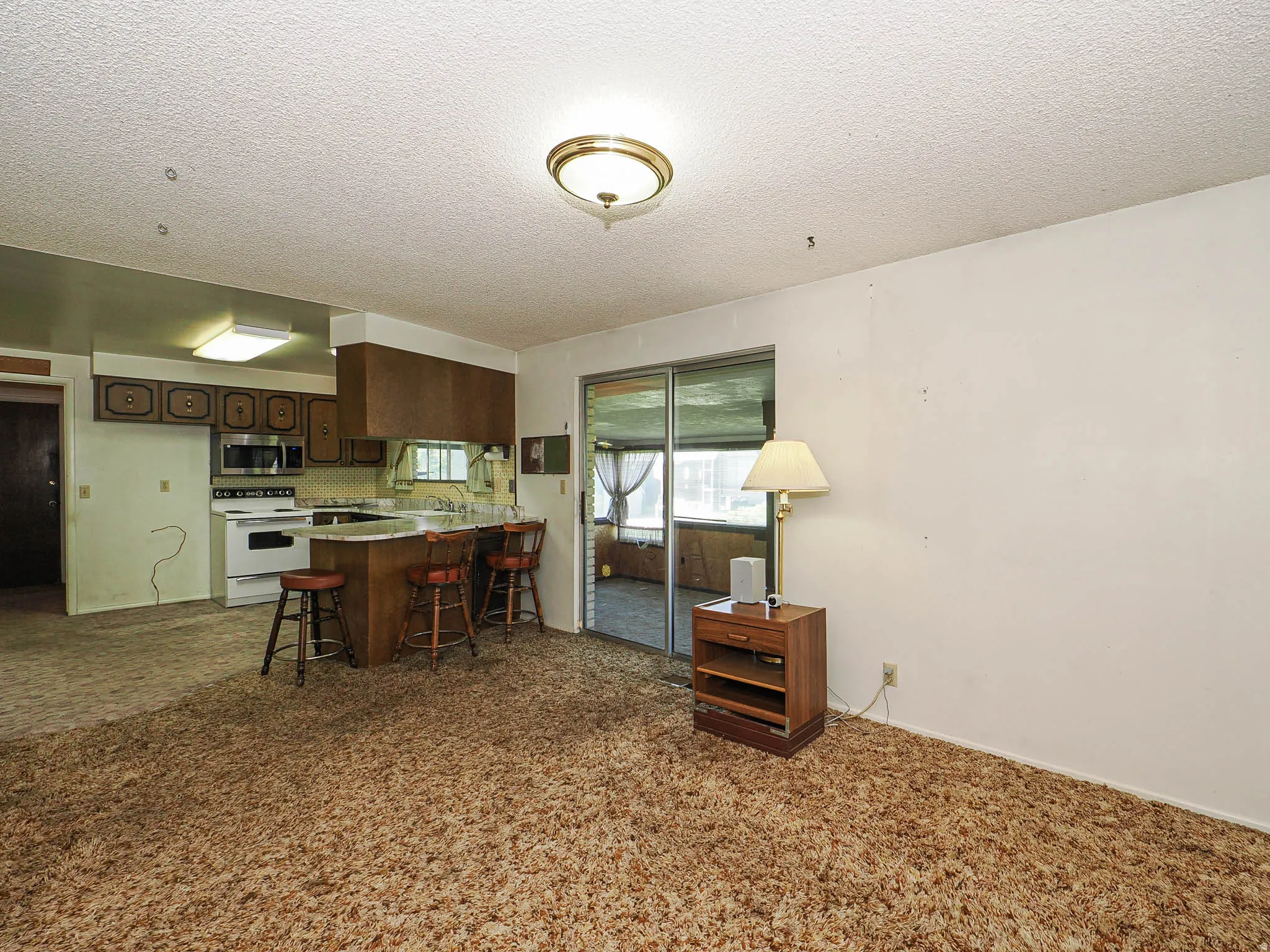 Open concept living space featuring a kitchen with wood cabinetry and white appliances, a breakfast bar, and sliding glass doors