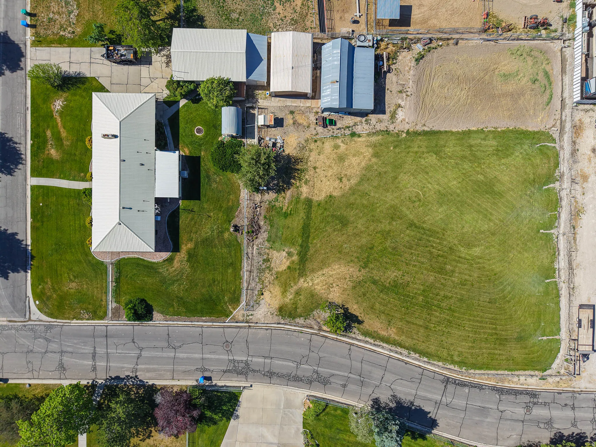 Expansive corner lot featuring a main residence with a light-colored roof, multiple outbuildings, and a substantial grassed area