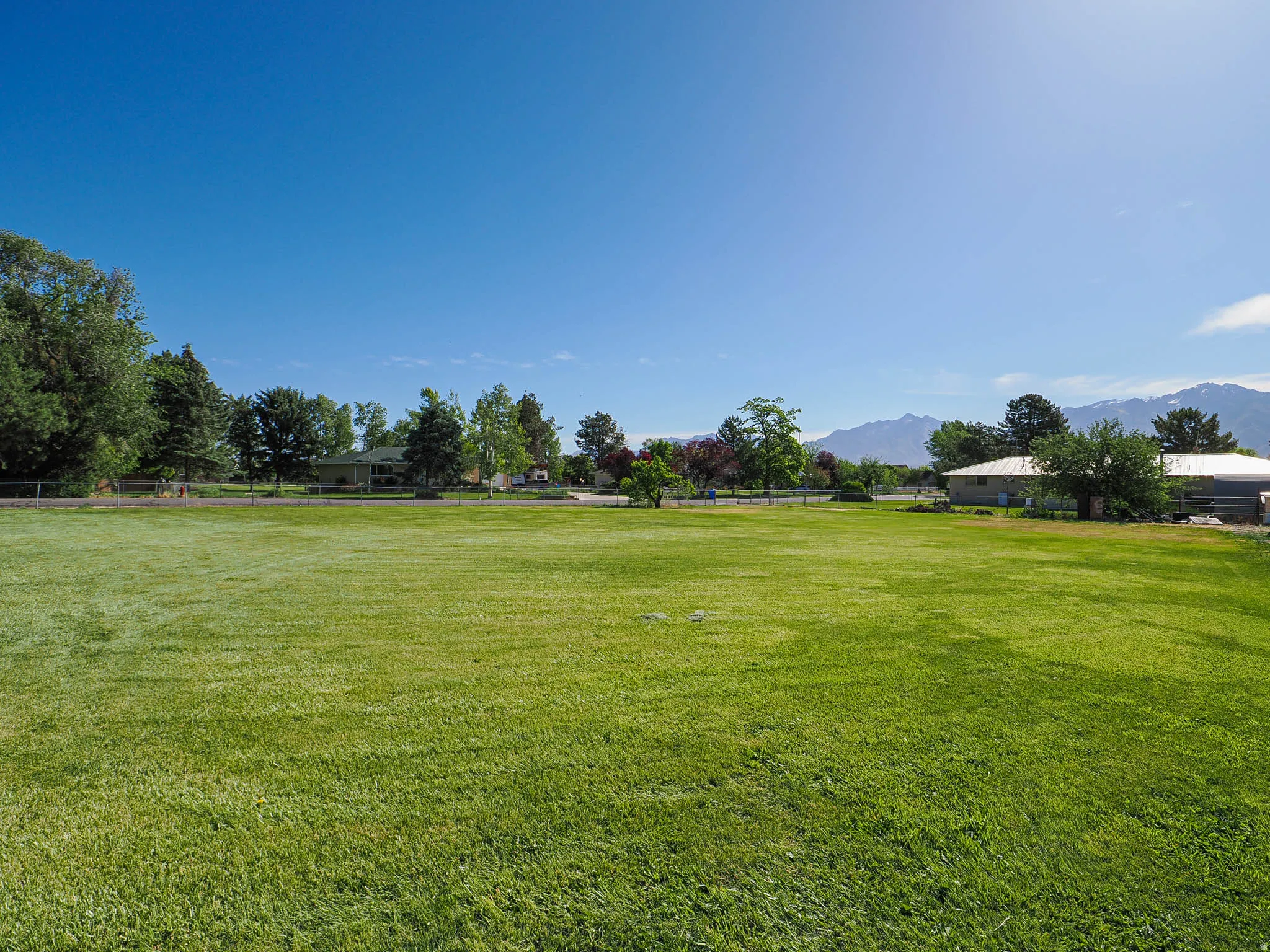 Expansive grass field with distant mountainous terrain, surrounded by mature trees and residential structures