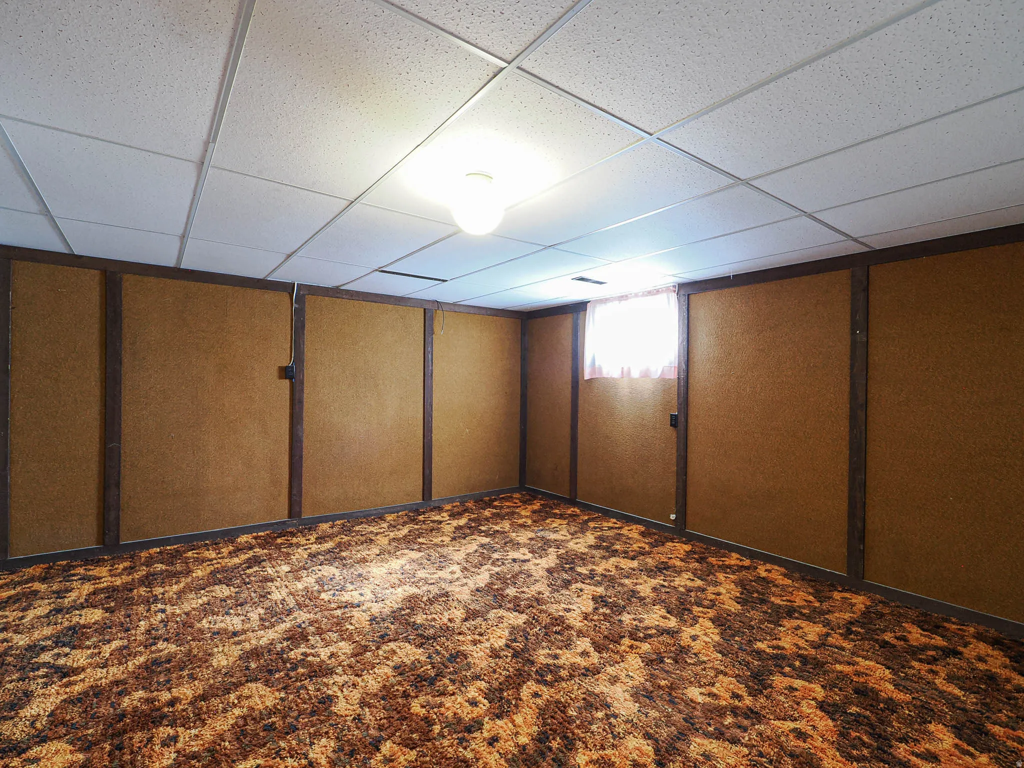 Expansive interior space featuring a drop ceiling, a single ceiling-mounted light fixture, and a window with a sheer curtain