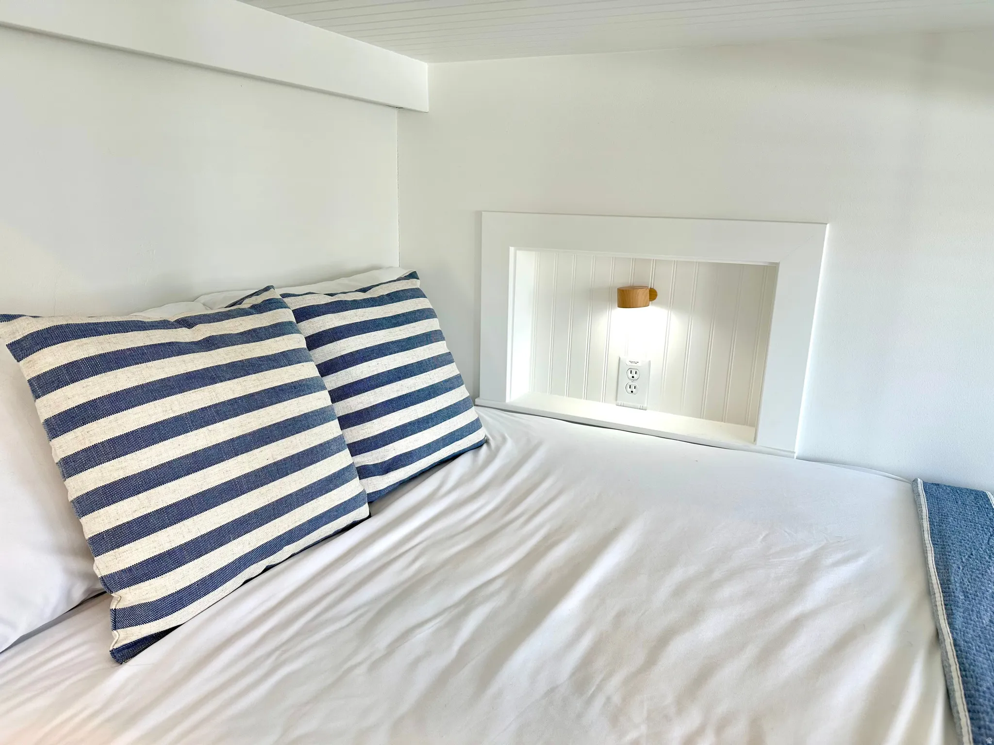 Built-in bunk bed with an integrated recessed niche featuring wood-finish wall paneling, a wall-mounted light fixture, and a power outlet