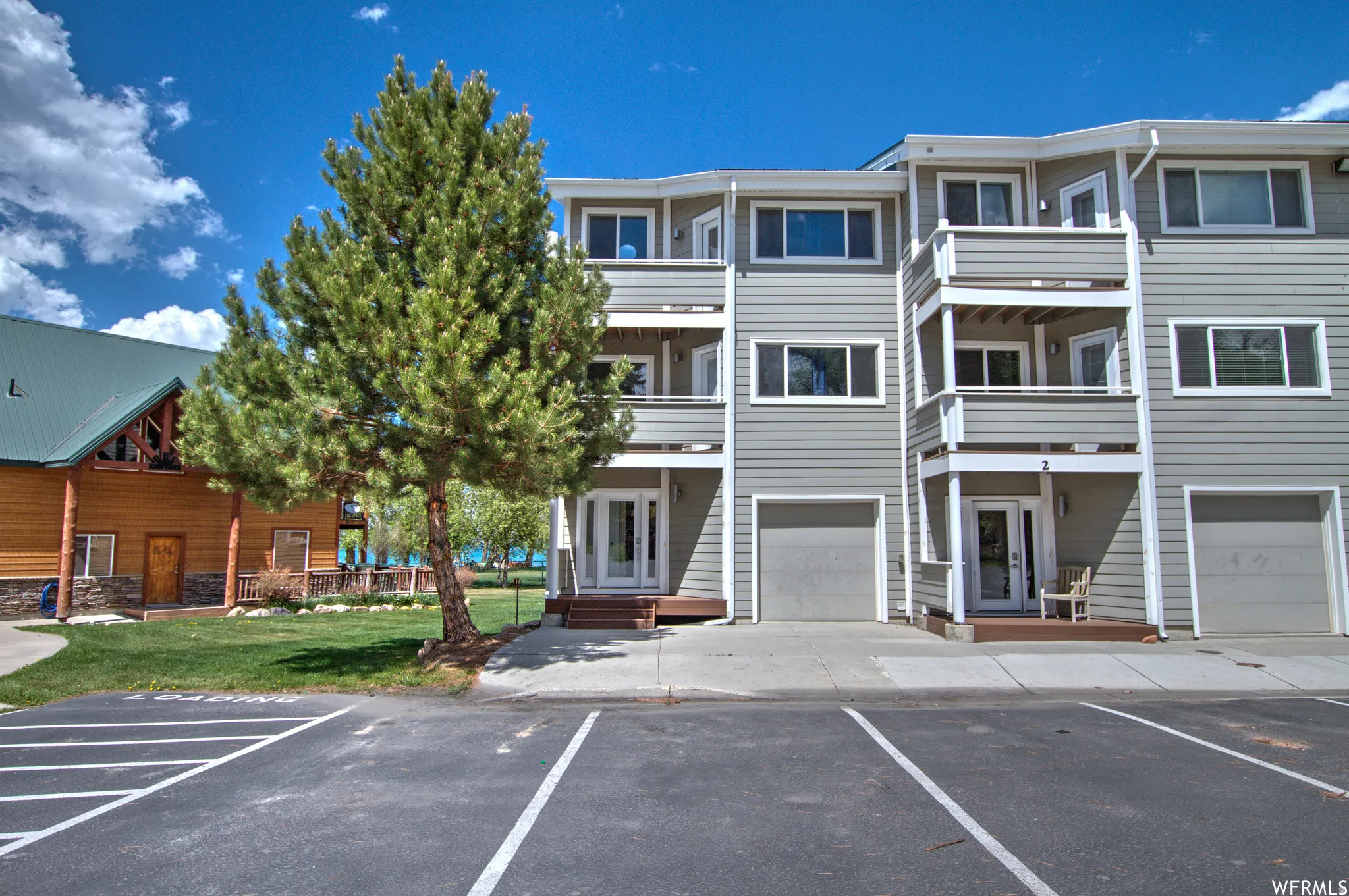 Multi-story building featuring light gray siding, white trim, and individual ground-level garages