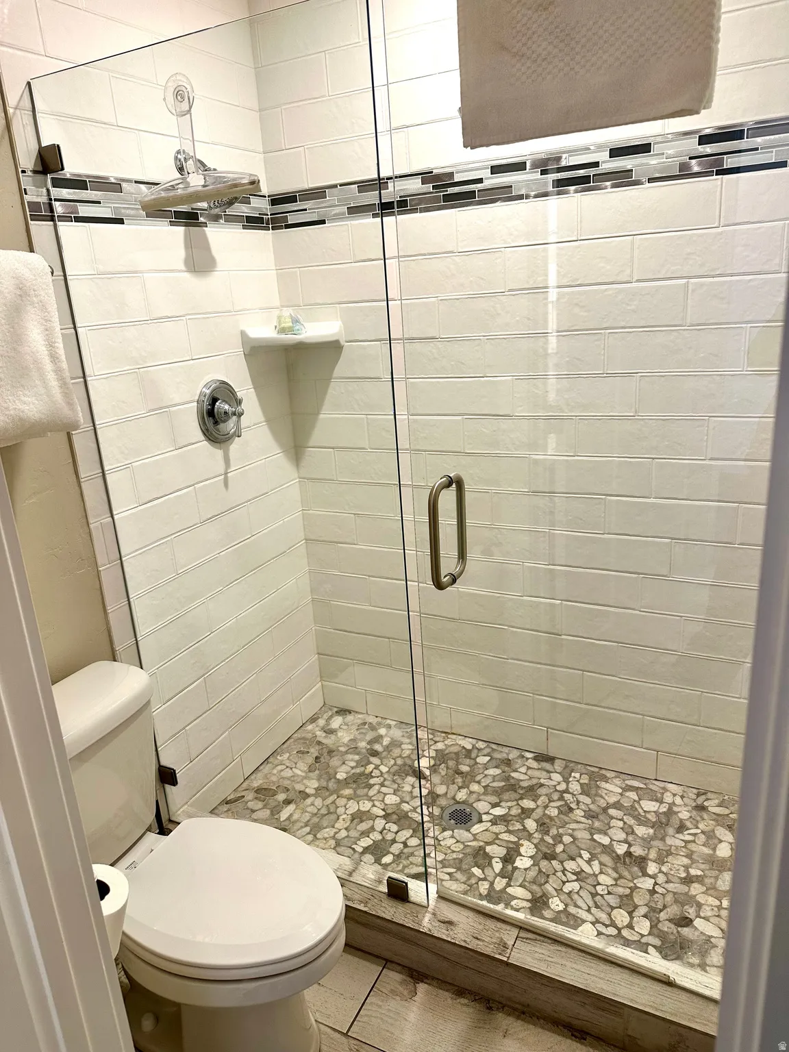 Walk-in shower with clear glass enclosure and pebble-tiled floor