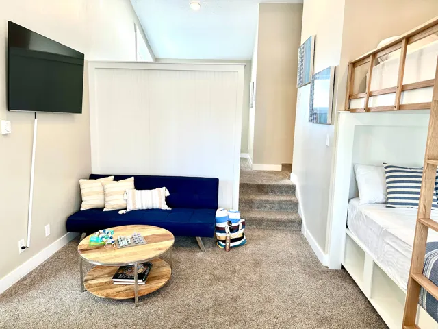 Carpeted living area featuring a wall-mounted television, built-in bunk beds with integrated storage, and a partial wall with vertical paneling