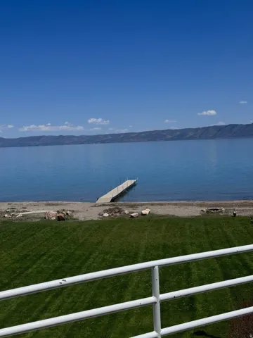 Expansive waterfront property featuring a private dock, a manicured lawn, a gravel beach, and distant mountain scenery