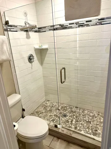 Walk-in shower with clear glass enclosure and pebble-tiled floor