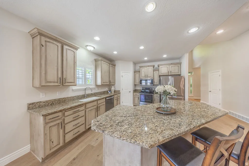 Kitchen featuring an island with granite countertop, light wood-finish flooring, recessed lighting, distressed cabinetry, and stainless steel appliances