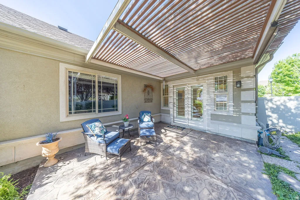 Expansive stamped concrete patio featuring a louvered pergola, stucco exterior, sliding glass door, and a large picture window