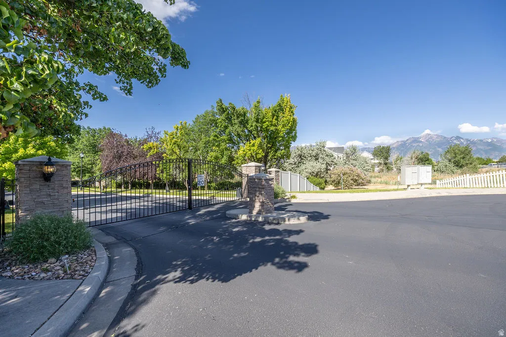 Wrought iron entry gate with stone pillars featuring exterior sconces, leading to a paved driveway