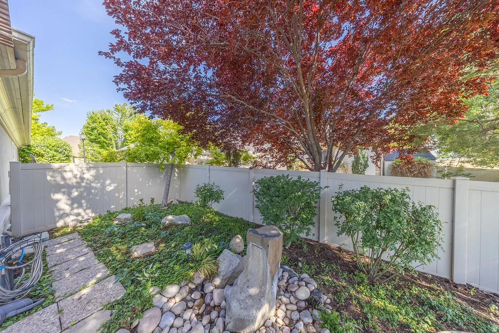 Landscaped garden area featuring a mature red-leaf tree, a stone pathway, decorative river rock accents, and established green plantings