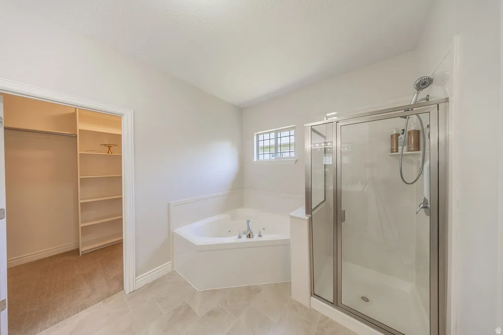 Bathroom featuring a corner soaking tub with deck-mounted fixtures, a glass-enclosed shower with a handheld showerhead, and light-toned tile flooring