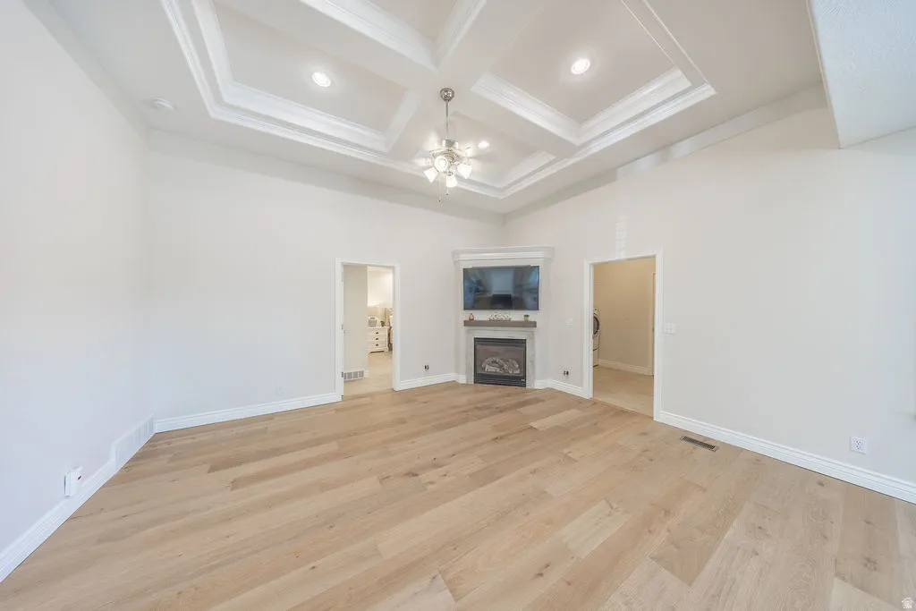 Spacious room featuring light wood-finish flooring and a multi-tiered tray ceiling with recessed lighting