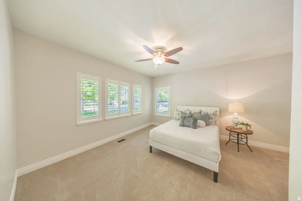 Carpeted room featuring a ceiling fan with light fixture, four windows with plantation shutters, light-toned walls, and white baseboards
