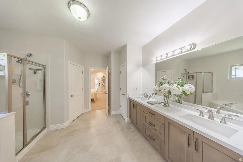 Spacious bathroom featuring a dual vanity with light wood-finish cabinetry, a large frameless mirror, and a walk-in shower with a glass enclosure