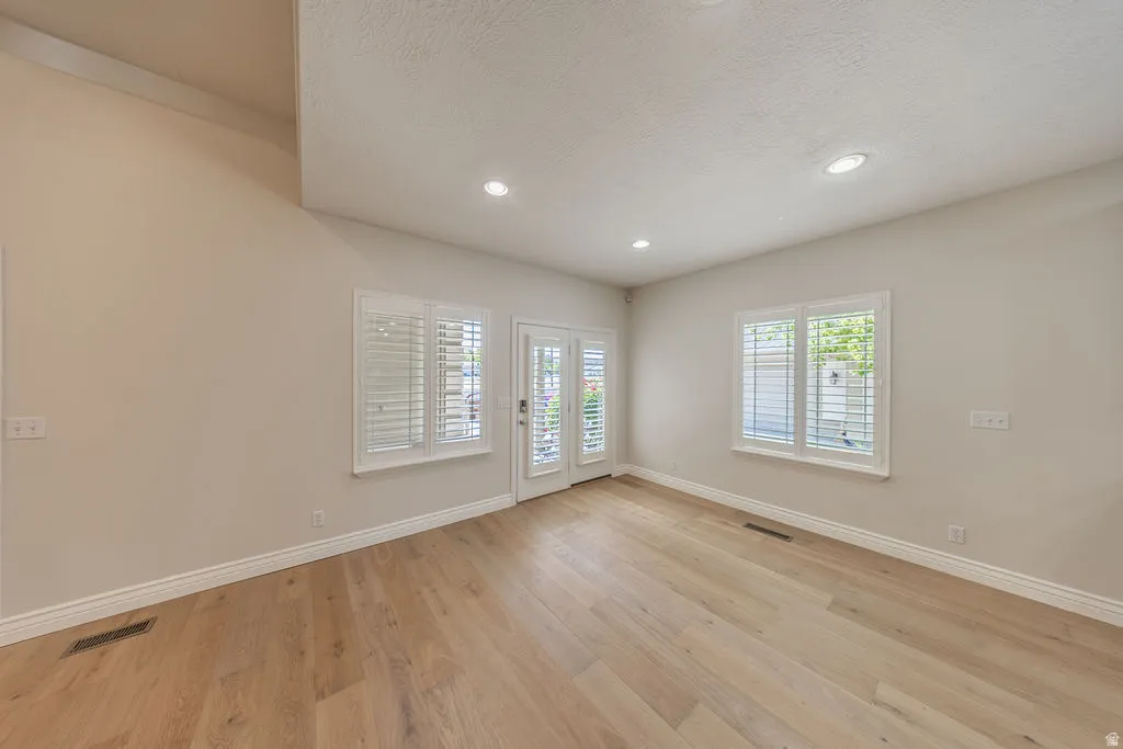 Spacious room with wood-finish flooring, two windows with white plantation shutters, and a French door with a matching shutter system
