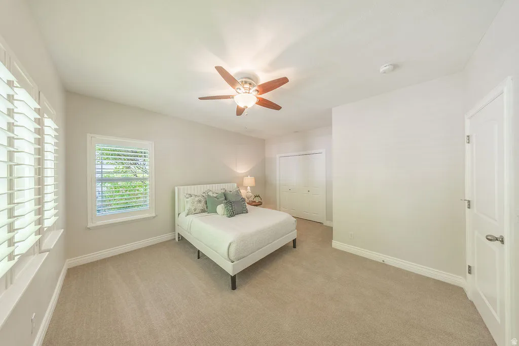 Light-filled room featuring neutral-toned carpeting, a ceiling fan with integrated lighting, and white plantation shutters on multiple windows