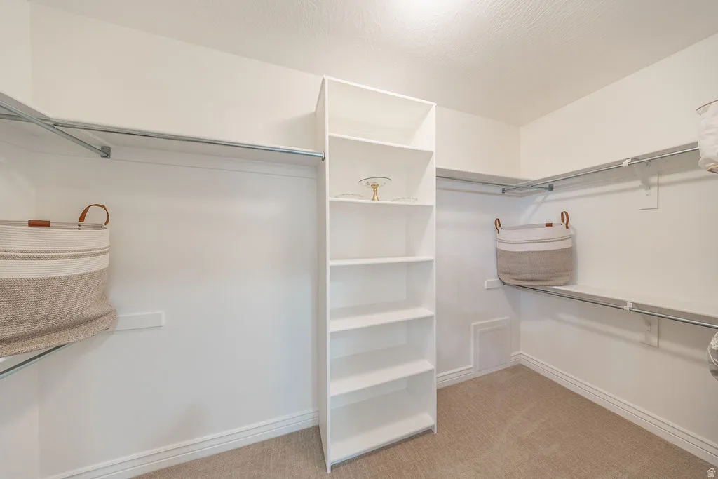 Walk-in closet featuring built-in shelving, white walls, light-colored carpet, and wall-mounted hanging rods