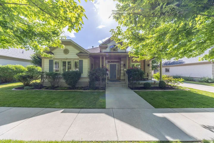Single-story residence featuring a covered front porch with columns, a prominent bay window with shutters, a concrete walkway, and a manicured lawn with mature trees