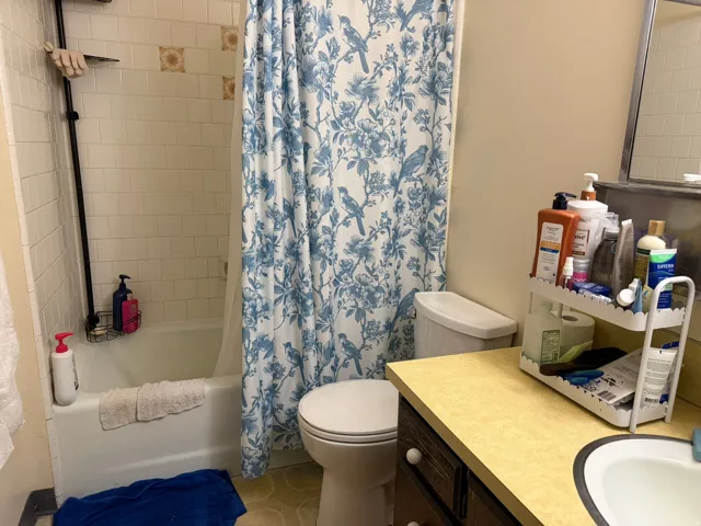 Bathroom featuring a white bathtub, white tile surround with decorative accents, a toilet, a vanity with a light-colored countertop, and dark wood cabinetry