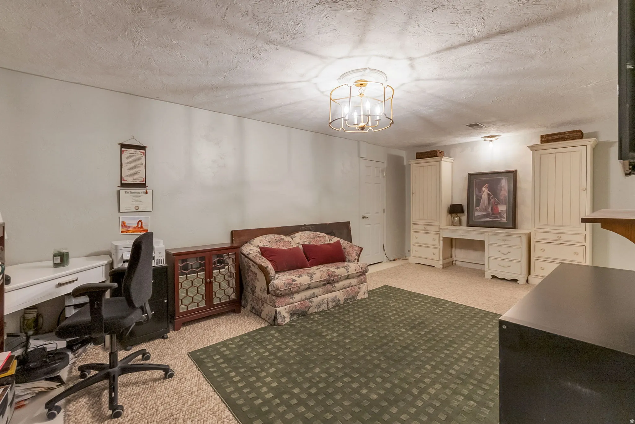 Recessed lighting and a decorative ceiling fixture illuminate a room featuring light-colored walls and textured carpeting