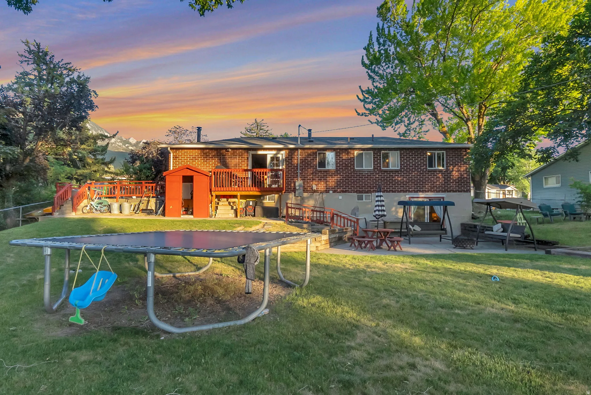 Expansive backyard featuring a manicured lawn, an upper-level wood deck, a lower-level concrete patio, a brick exterior, and a storage shed