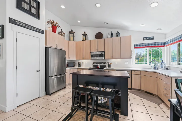 Spacious kitchen featuring an island with seating, stainless steel appliances, light-toned cabinetry, light countertops, and tile flooring