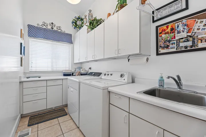 Bright utility room featuring ample white cabinetry, integrated sink, and a window with white blinds