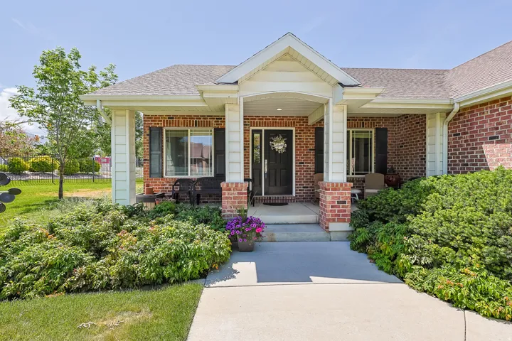 Brick facade home with a covered front porch, white columns, a dark entry door, and manicured shrubbery