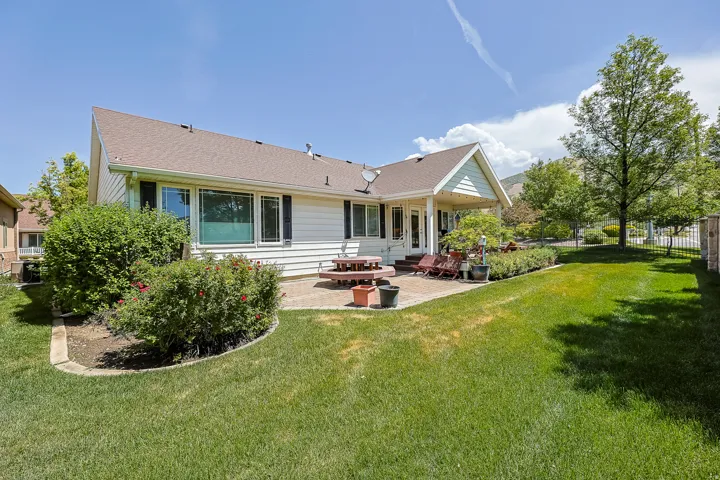 Expansive rear yard featuring a covered patio, a manicured lawn, established landscaping, and mature trees
