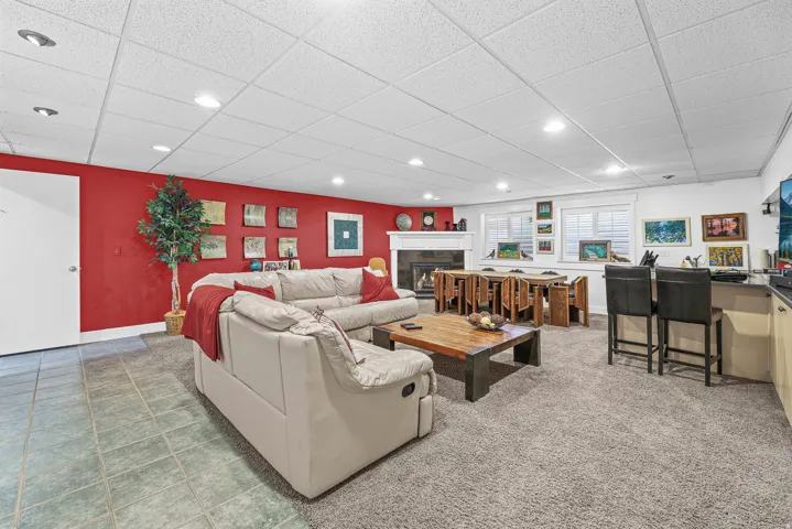 Open-concept living space with recessed lighting, a built-in wet bar, a fireplace with a white mantel, and multiple windows with white shutters